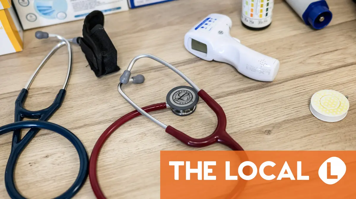 Medical equipment including two stethoscopes and a digital thermometer on a wooden table with a news logo overlay.