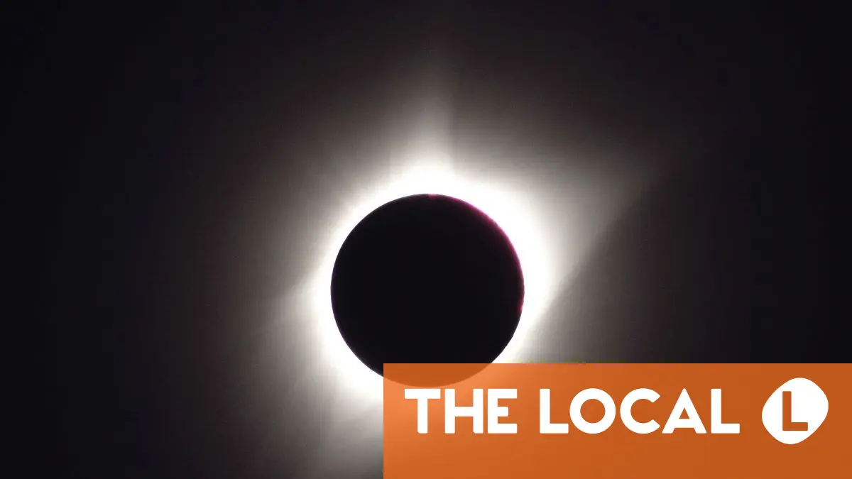 A silhouette of a solar eclipse against a bright sun with a logo in the corner.