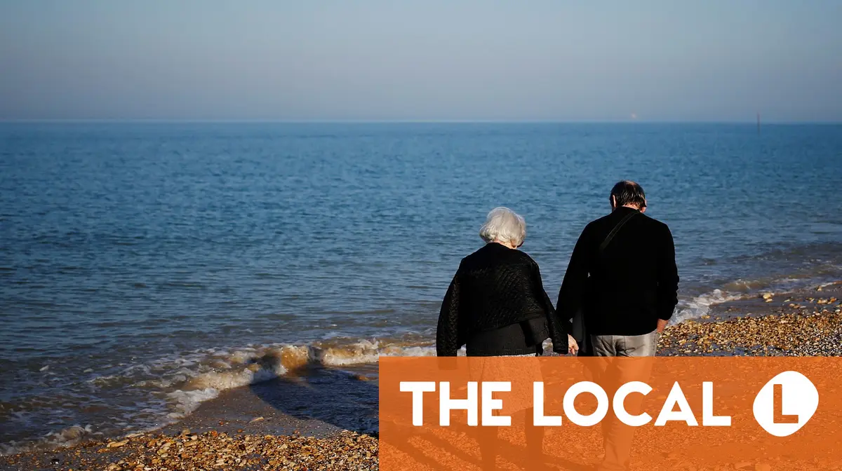 Two people standing on a pebble beach looking at the ocean.