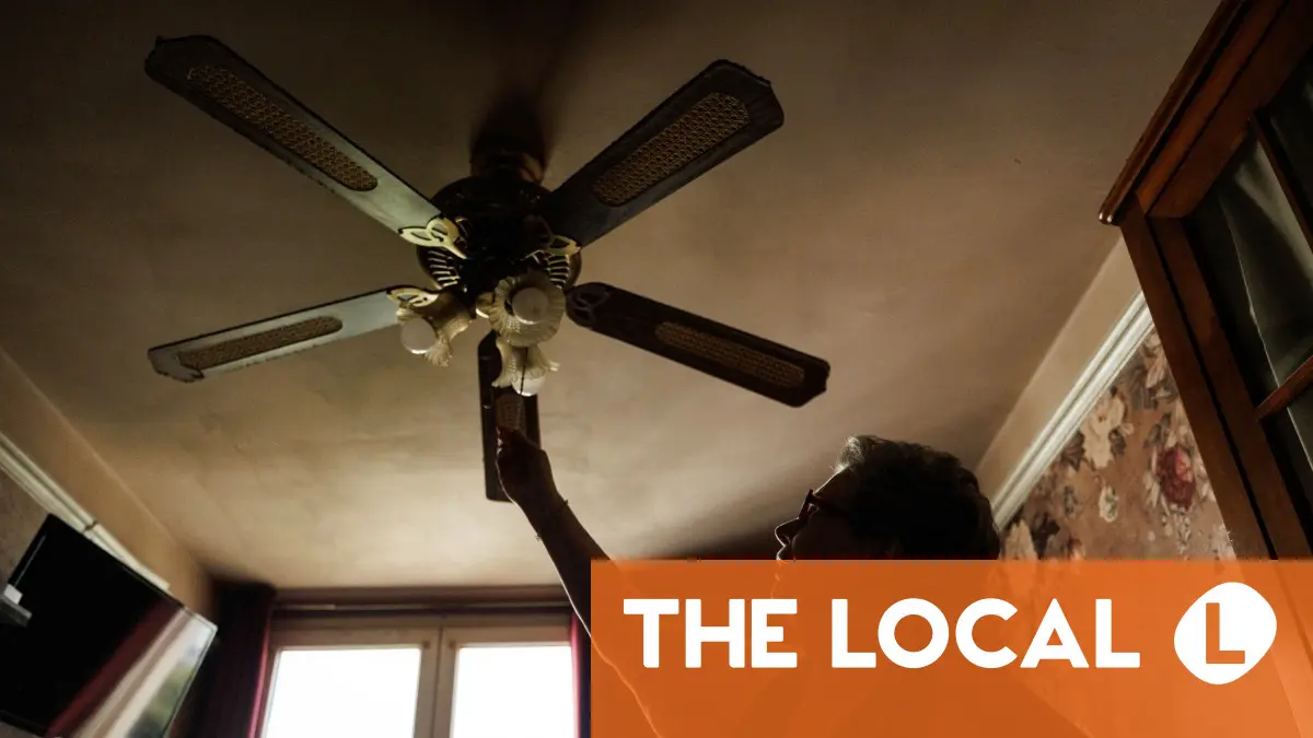 A person reaches up to adjust a ceiling fan in a room with patterned wallpaper.
