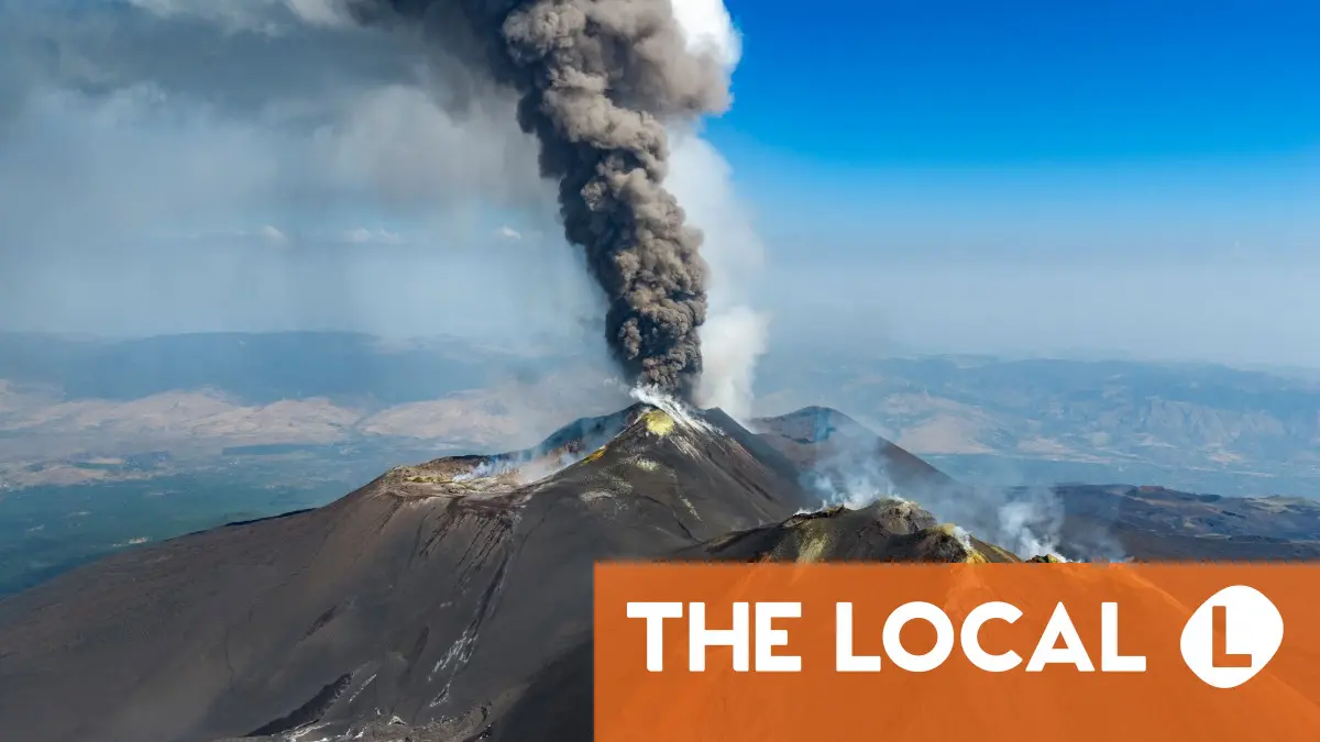 A large volcano emitting a thick plume of dark smoke.