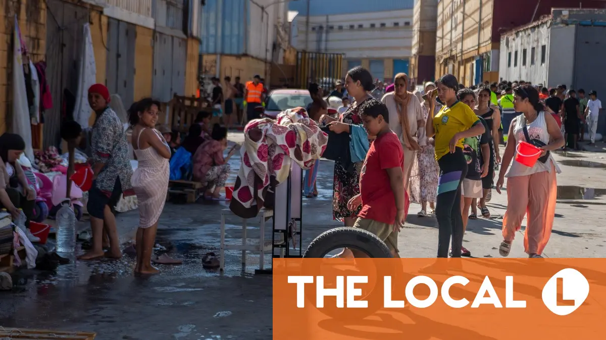 A crowd of people gathered outdoors near stacked items and buildings.