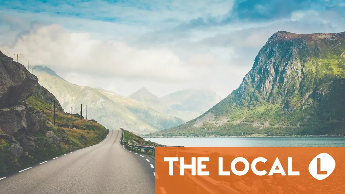 A winding road passes through a lush, mountainous landscape next to a body of water.
